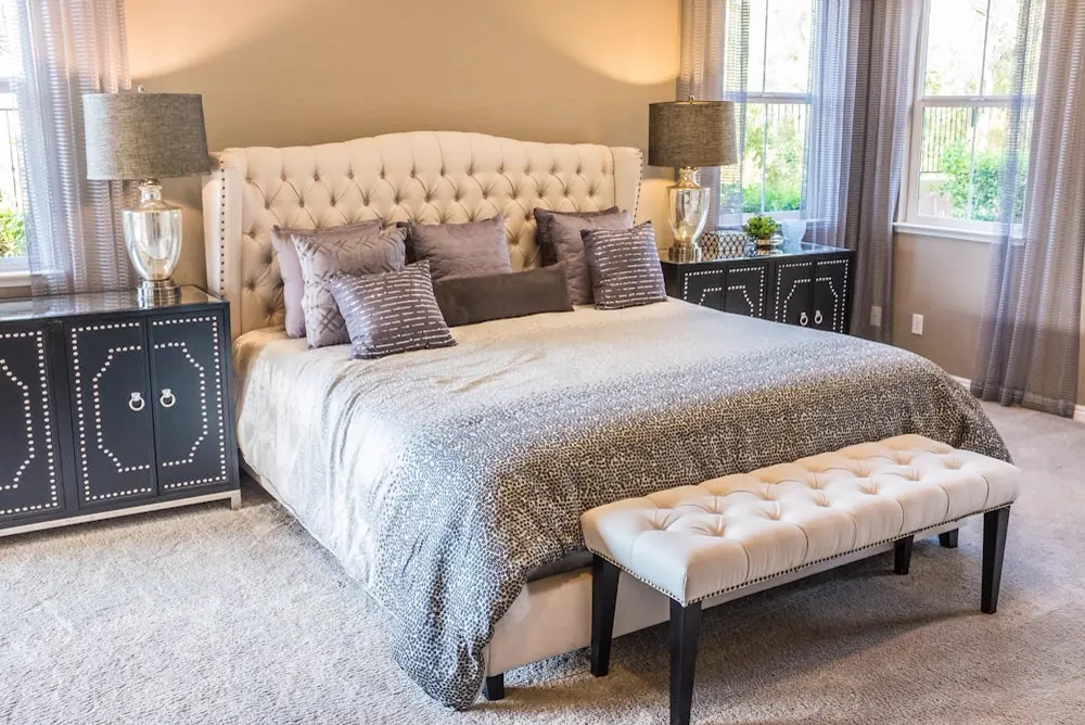 A serene bedroom with a tufted bed, side lamps, deep curtains and matching bench